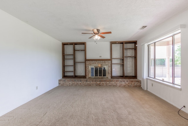 unfurnished living room with ceiling fan, light colored carpet, a fireplace, and a textured ceiling