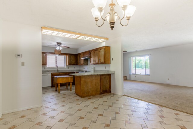 kitchen with hanging light fixtures, kitchen peninsula, white appliances, light colored carpet, and ceiling fan with notable chandelier