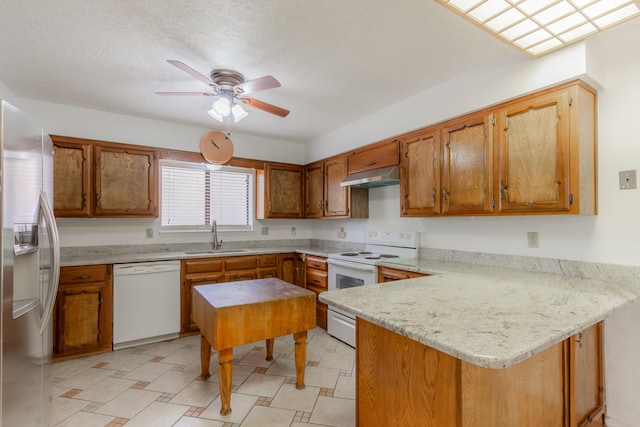 kitchen featuring sink, kitchen peninsula, white appliances, light stone countertops, and ceiling fan