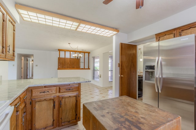 kitchen featuring stainless steel refrigerator with ice dispenser, kitchen peninsula, ceiling fan with notable chandelier, and light stone countertops