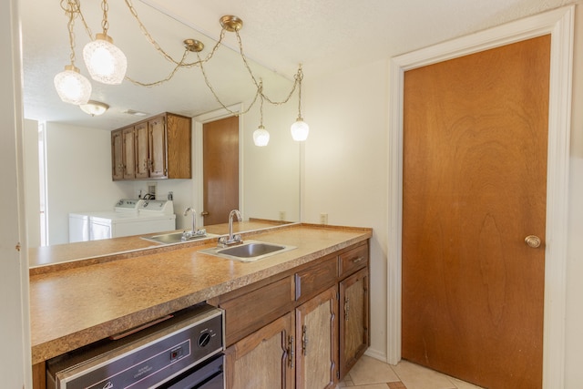 kitchen with pendant lighting, light tile patterned flooring, sink, stainless steel dishwasher, and washer and clothes dryer