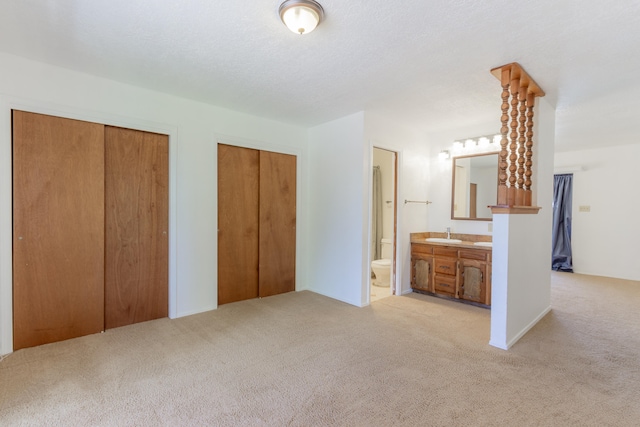 unfurnished bedroom with a textured ceiling, ensuite bathroom, sink, light colored carpet, and multiple closets