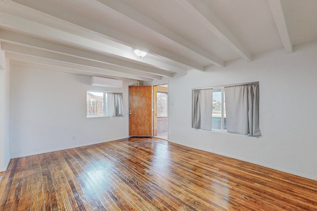 unfurnished room featuring beamed ceiling, a healthy amount of sunlight, an AC wall unit, and hardwood / wood-style floors