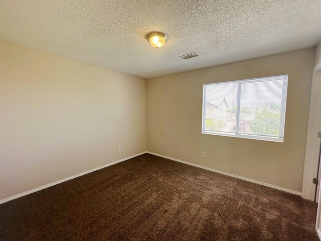 unfurnished room with dark carpet and a textured ceiling