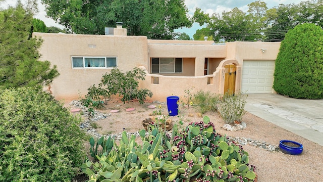 pueblo revival-style home featuring an attached garage, driveway, a chimney, and stucco siding