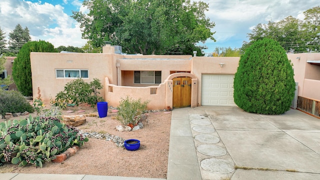 pueblo-style home with an attached garage, fence, concrete driveway, stucco siding, and a chimney