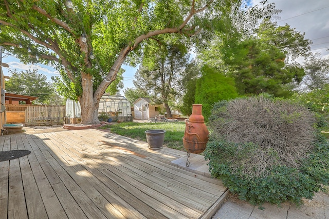 wooden deck with a storage unit, an outdoor structure, and fence