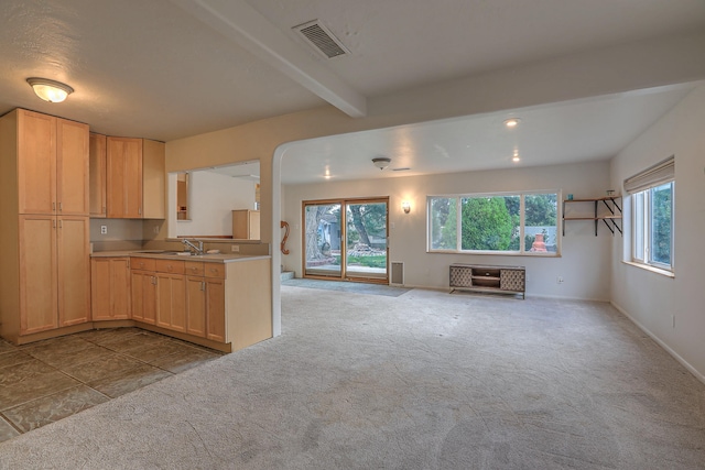 kitchen featuring beam ceiling, light brown cabinets, sink, and light carpet