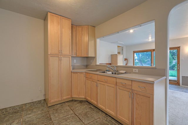 kitchen with kitchen peninsula, light brown cabinets, a textured ceiling, and sink