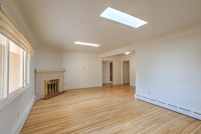 unfurnished living room featuring baseboard heating, a skylight, light hardwood / wood-style floors, and a tile fireplace