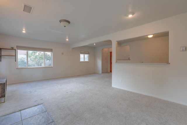 empty room featuring light colored carpet, visible vents, arched walkways, and baseboards