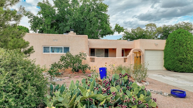 pueblo-style house featuring an attached garage, a chimney, concrete driveway, and stucco siding