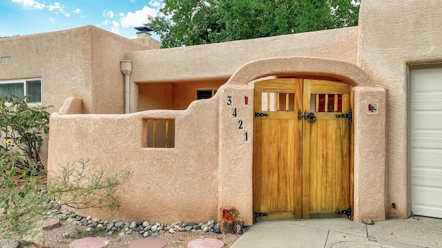 property entrance featuring a garage, a gate, a chimney, and stucco siding