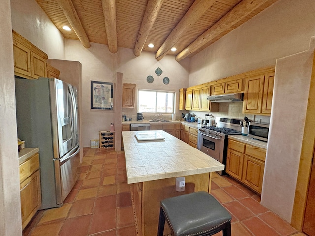 kitchen with beamed ceiling, tile countertops, a kitchen bar, stainless steel appliances, and a center island