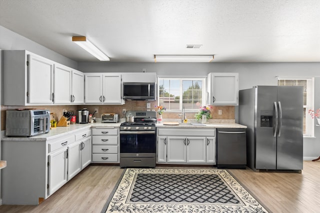 kitchen featuring white cabinets, light hardwood / wood-style floors, appliances with stainless steel finishes, and a textured ceiling