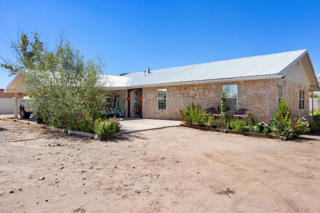 rear view of house featuring a patio, metal roof, and stone siding