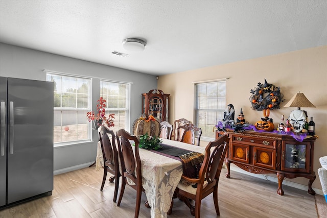 dining room featuring light wood-style floors, a textured ceiling, visible vents, and a wealth of natural light
