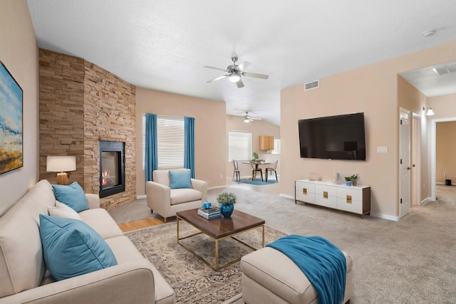 carpeted living room featuring a textured ceiling, vaulted ceiling, ceiling fan, and a stone fireplace