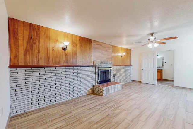 unfurnished living room featuring a fireplace, light hardwood / wood-style flooring, brick wall, ceiling fan, and a textured ceiling