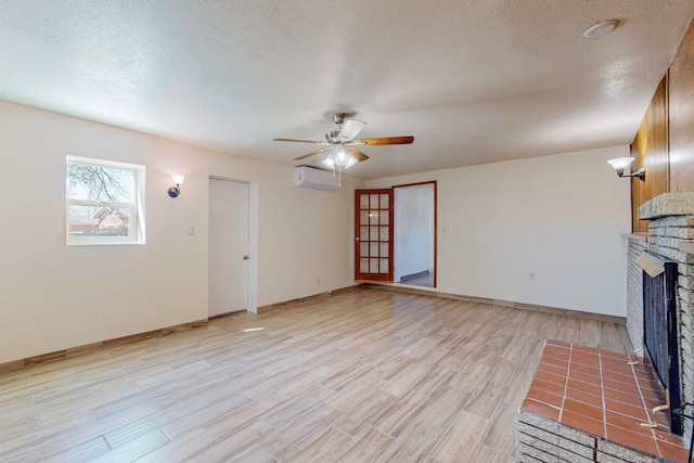 unfurnished living room with a textured ceiling, a brick fireplace, ceiling fan, a wall unit AC, and light wood-type flooring