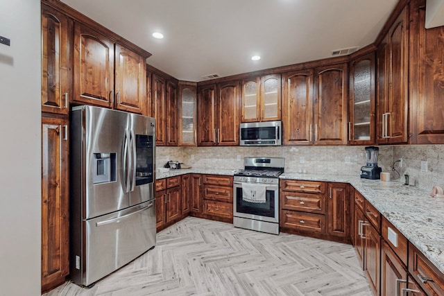 kitchen with light parquet flooring, light stone countertops, appliances with stainless steel finishes, and tasteful backsplash