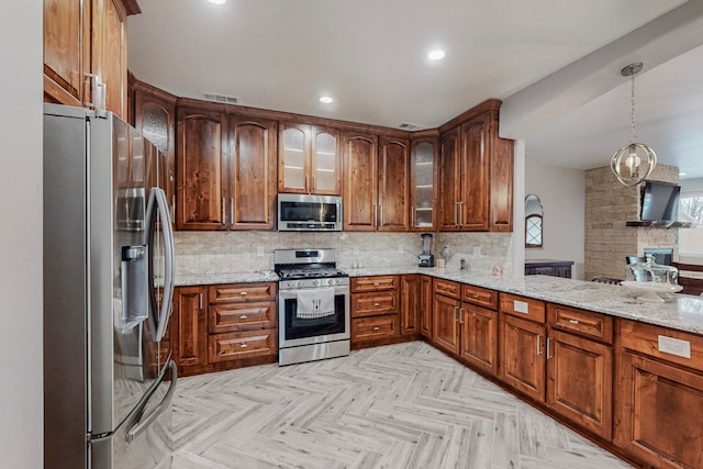 kitchen featuring appliances with stainless steel finishes, light stone counters, hanging light fixtures, and tasteful backsplash