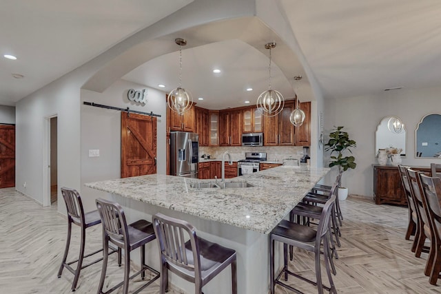 kitchen with a barn door, appliances with stainless steel finishes, light stone countertops, sink, and light parquet floors