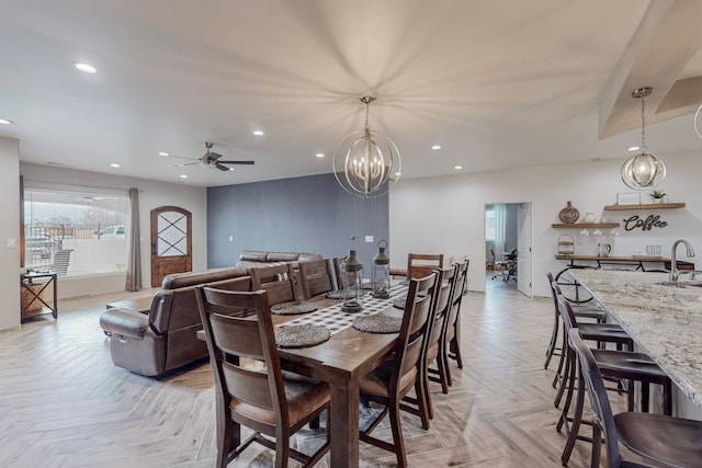 dining area with sink, ceiling fan with notable chandelier, and light parquet flooring