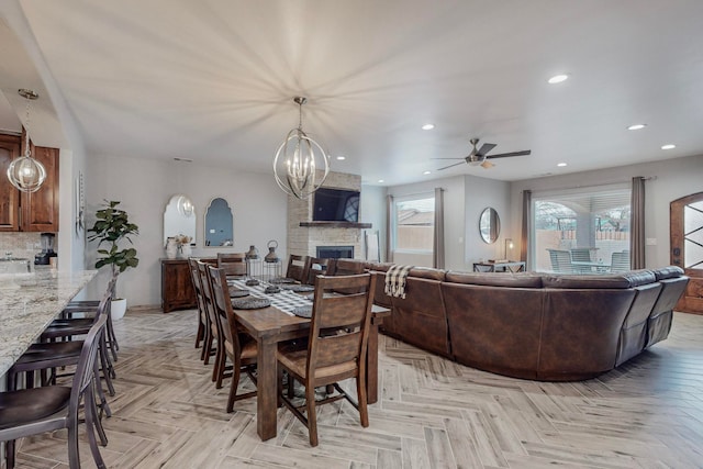 dining area with ceiling fan with notable chandelier, light parquet flooring, and a fireplace