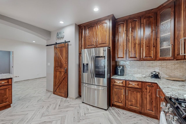 kitchen featuring tasteful backsplash, stainless steel appliances, light stone countertops, light parquet floors, and a barn door