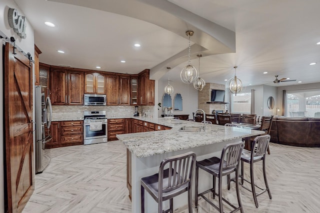 kitchen with a kitchen bar, a sink, tasteful backsplash, a barn door, and appliances with stainless steel finishes