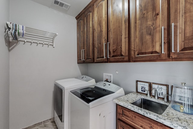 clothes washing area with visible vents, washer and clothes dryer, a sink, cabinet space, and baseboards