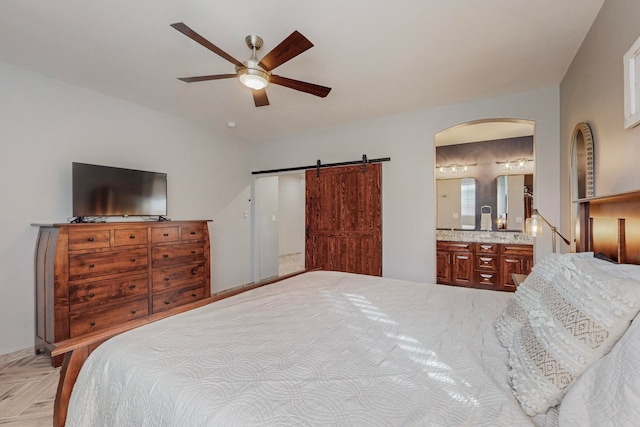 bedroom featuring a barn door, ceiling fan, light parquet flooring, and ensuite bath