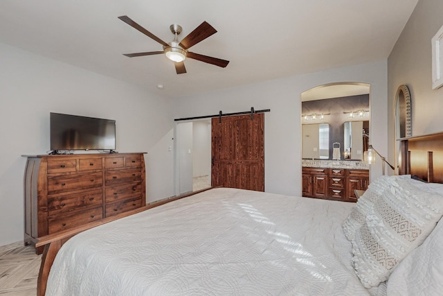 bedroom with arched walkways, connected bathroom, a barn door, and ceiling fan