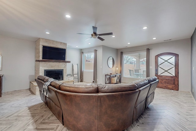 living room featuring ceiling fan, light parquet floors, and a stone fireplace