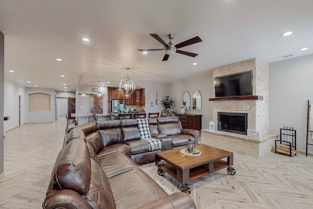 living room featuring a fireplace, light parquet flooring, and ceiling fan with notable chandelier