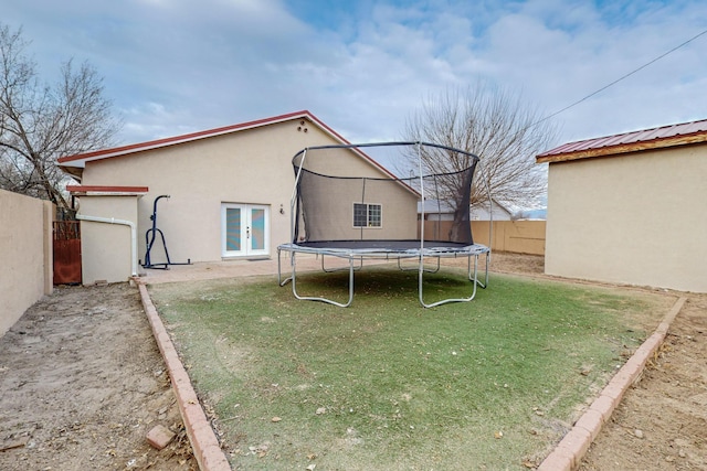 view of yard with a trampoline, french doors, and fence