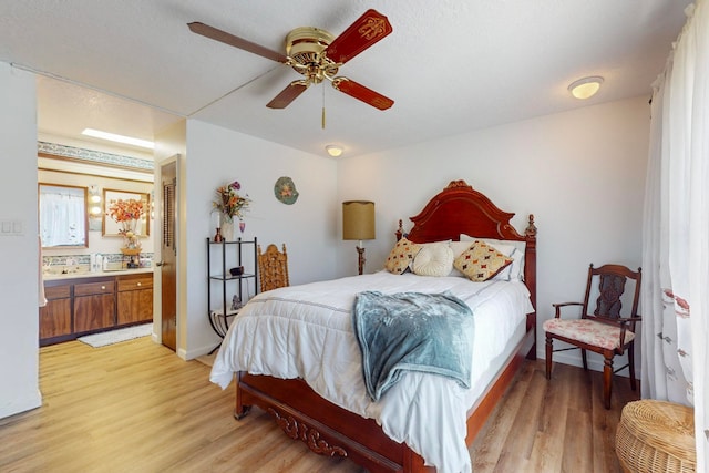 bedroom with a textured ceiling, ceiling fan, light wood-type flooring, and connected bathroom