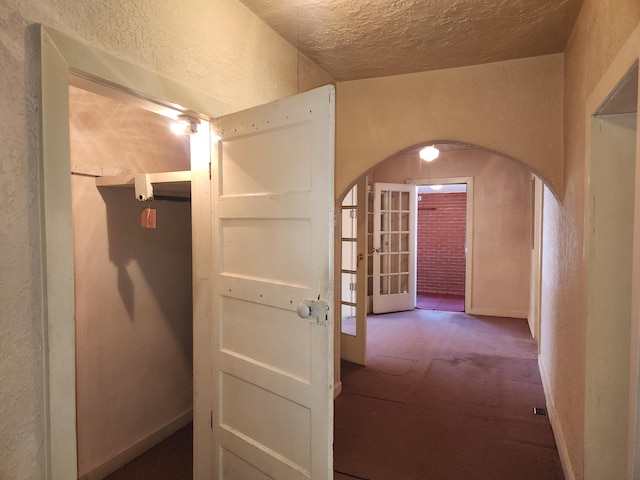 hall featuring a textured ceiling, carpet floors, and french doors