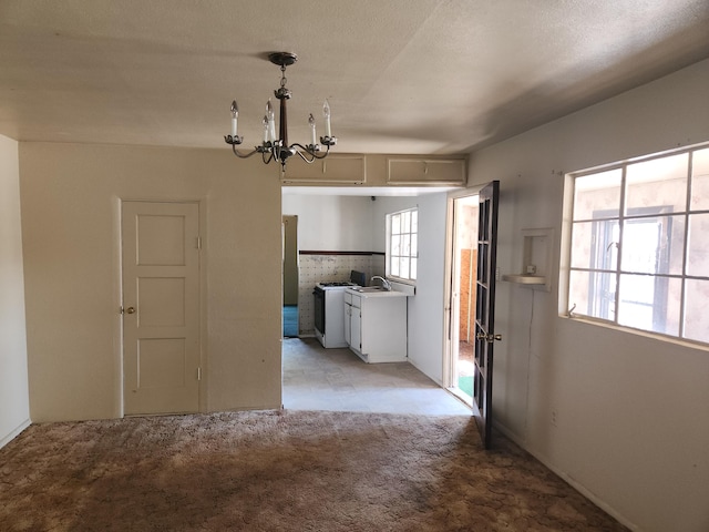 interior space featuring a textured ceiling, light colored carpet, an inviting chandelier, hanging light fixtures, and white cabinets