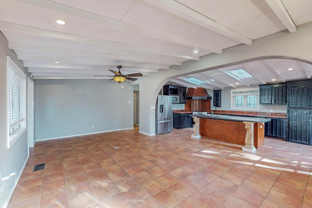 kitchen featuring lofted ceiling with beams, ceiling fan, a center island, and stainless steel fridge