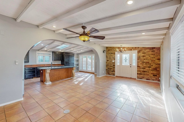 kitchen featuring a breakfast bar, beamed ceiling, ceiling fan with notable chandelier, light tile patterned floors, and brick wall