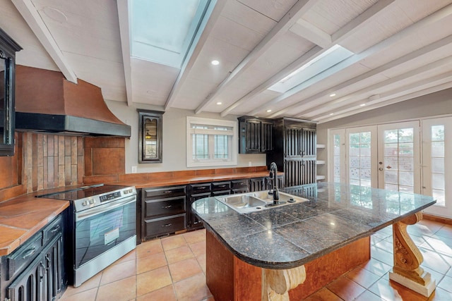 kitchen featuring stainless steel electric stove, lofted ceiling with beams, a breakfast bar area, a kitchen island with sink, and sink