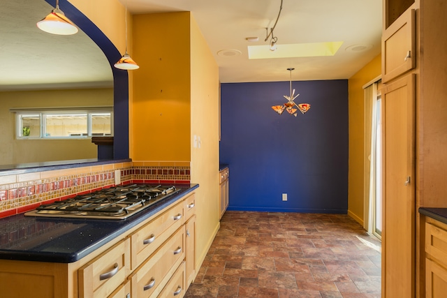 kitchen with a skylight, stainless steel gas stovetop, light brown cabinetry, pendant lighting, and tasteful backsplash