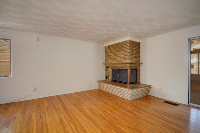 unfurnished living room featuring a brick fireplace, crown molding, and hardwood / wood-style floors