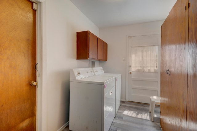 laundry room with washing machine and clothes dryer, cabinets, and light wood-type flooring