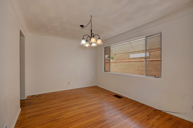 spare room with wood-type flooring and an inviting chandelier