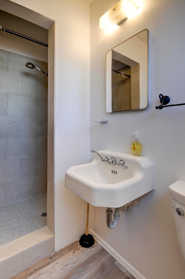 bathroom featuring wood-type flooring, toilet, and tiled shower