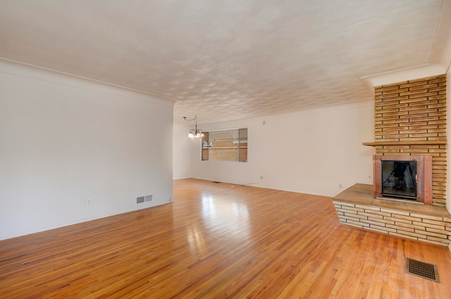 unfurnished living room with an inviting chandelier, a fireplace, and light hardwood / wood-style flooring