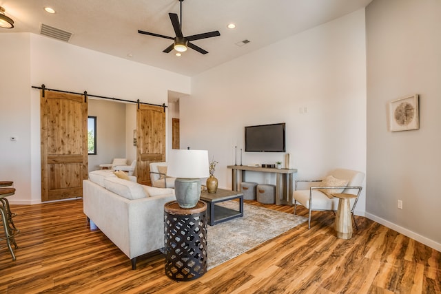 living room featuring a barn door, ceiling fan, a towering ceiling, and hardwood / wood-style floors